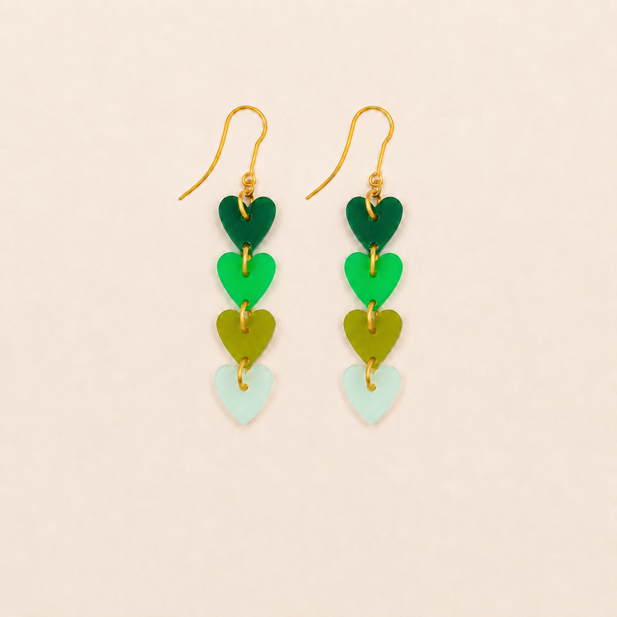 Pair of earrings with heart-shaped green and gold components on a beige background