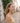 Woman in a yellow top standing on a cobblestone street with white buildings and greenery.