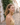 Woman in a yellow top standing on a cobblestone street with white buildings and greenery.