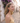 Woman with red earrings standing on a cobblestone street with purple flowers in the background