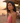 Woman in a pink top standing on a beach at sunset with people in the background.