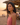 Woman in a pink top standing on a beach at sunset with people in the background.