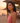 Woman in a pink top standing on a beach at sunset with people in the background.