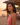 Woman in a pink top standing on a beach at sunset with people in the background.