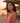 Woman in a pink top standing on a beach at sunset with people in the background.
