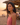 Woman in a pink top standing on a beach at sunset with people in the background.