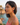 Woman wearing heart-shaped earrings with a scenic background of water and rocks.