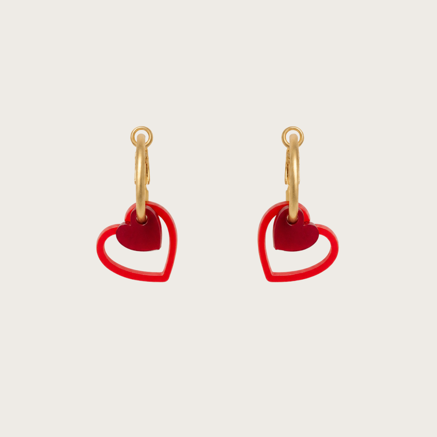 Gold hoop earrings with red heart charms on a beige background