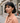 Woman with short black hair and a peach coat standing on a street.