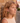 Woman with curly hair leaning against a stone wall in an outdoor setting