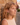 Woman with curly hair leaning against a stone wall in an outdoor setting