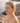 Woman with red earrings standing by a body of water with rocks.