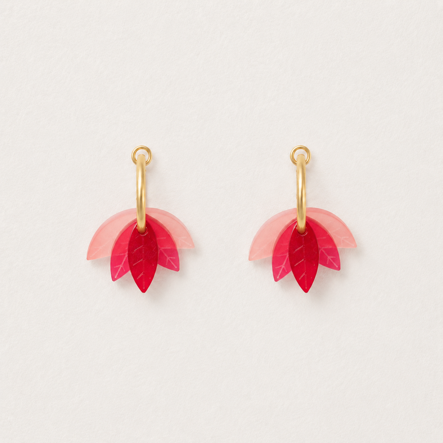 Pair of earrings with pink and red leaf-like charms on gold hooks against a light gray background