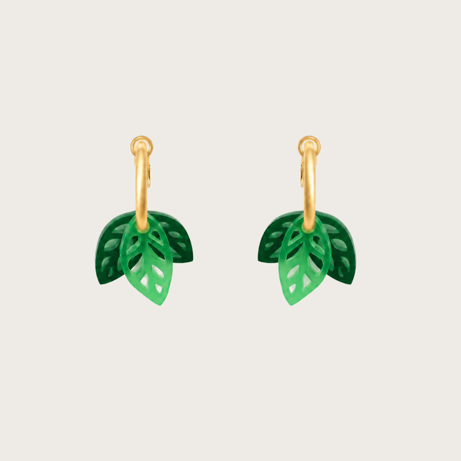 Green leaf-shaped earrings on gold hoops against a beige background