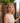 Woman with curly blonde hair standing outdoors near a stone wall and wooden gate.