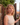 Woman with curly hair standing in front of a stone wall and wooden gate.